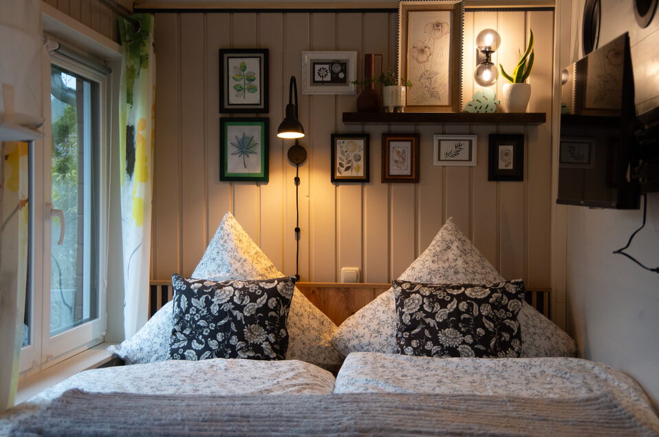 Gemütliches Doppelbett mit unterschiedlichen und vielen Kissen und Fenster mit Verdunklungsrollo