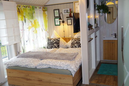 Bett mit zusätzlicher Decke, Blick auf den Eingang zum Bad mit Waschbecken bei geöffneter Glasschiebetür